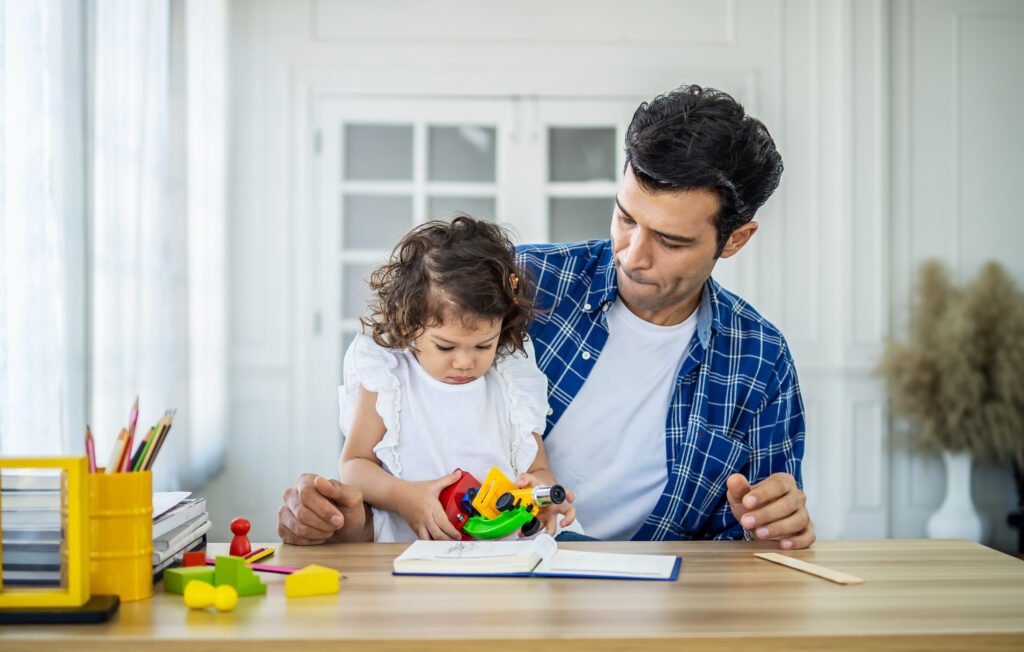 family, fatherhood and childhood concept - happy father and little daughter playing with toy microscope at table at home.